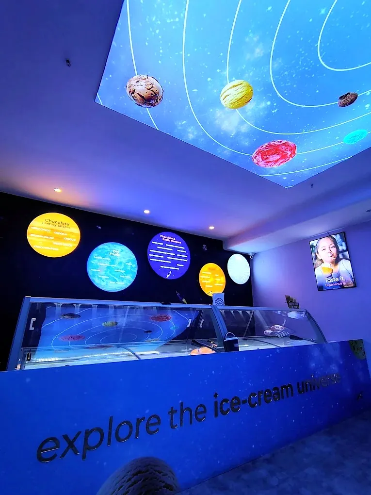 Snowball ice cream parlour in Wakad: a fabric light box of planets and ice creams in the ceiling, round glowing menu boards and the tagline on the counter