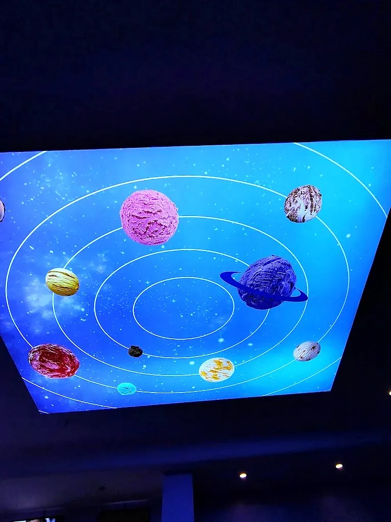 Close-up of the ceiling light box: planets made of ice cream scoops on a blue galaxy, printed on stretch fabric