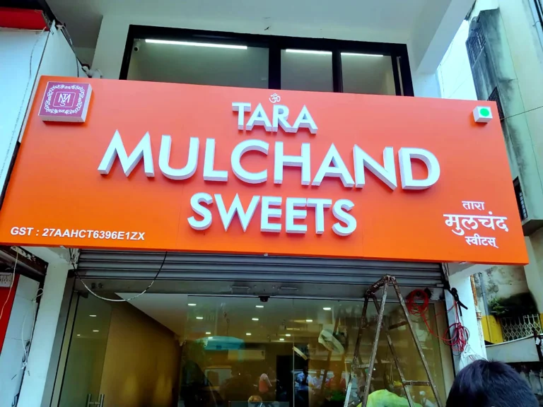 Tara Mulchand Sweets sign board: orange ACP base with raised white 3D acrylic letters TARA MULCHAND SWEETS, the logo in the top corner and the name in Marathi