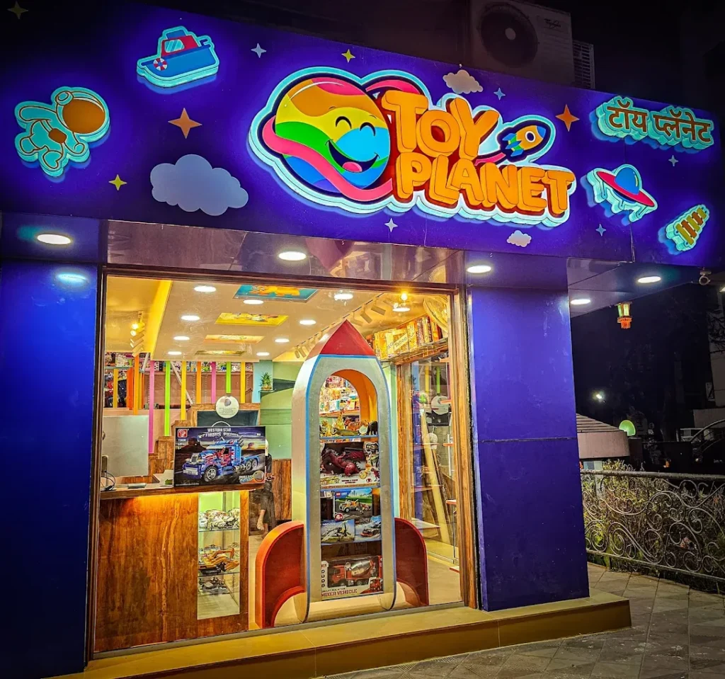 Toy Planet in Kalyani Nagar, Pune, at night: the TOY PLANET logo, the Marathi name and a collage of lit 3D acrylic shapes glowing on the blue fascia (photo from Toy Planet’s Google listing)