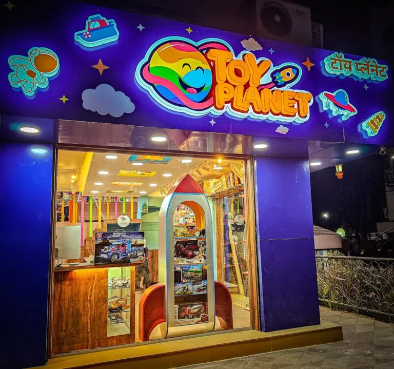 Toy Planet in Kalyani Nagar, Pune, at night: the TOY PLANET logo, the Marathi name and a collage of lit 3D acrylic shapes glowing on the blue fascia (photo from Toy Planet’s Google listing)
