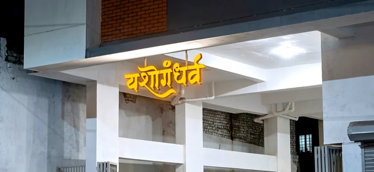 Yashogandharva LED letters glowing under the building entrance at dusk